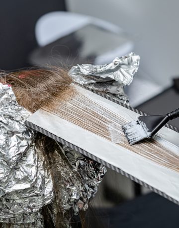 Hair stylist applying bleaching powder on clients hair and wrapping into the foil. Shatush